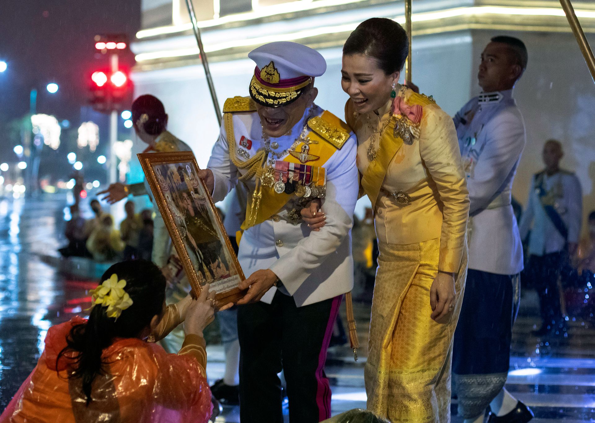 泰国国王哇集拉隆功和王后苏提达手拿普密蓬画像，与民众互动。（AP）