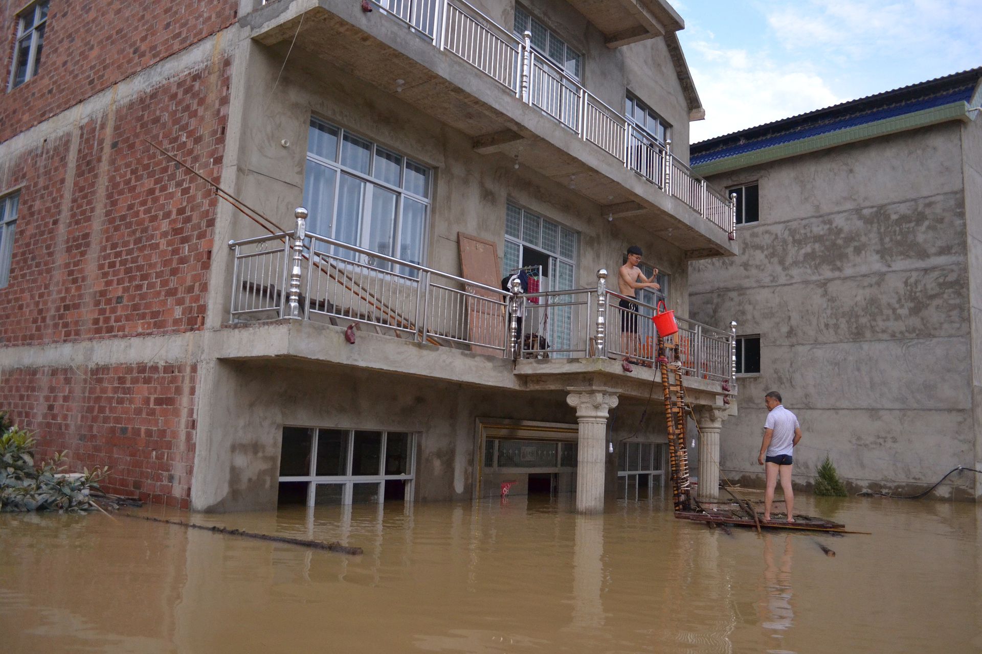 随着中国农村经济的发展，村民住房质量大幅提高，钢筋混净土的框架式楼房已经十分普遍。这避免了因洪水导致的房屋倒塌损失，大大降低了人员伤亡。图为7月12日，江西上饶鄱阳县村民正在从二楼阳台返回家中。  （人民视觉）