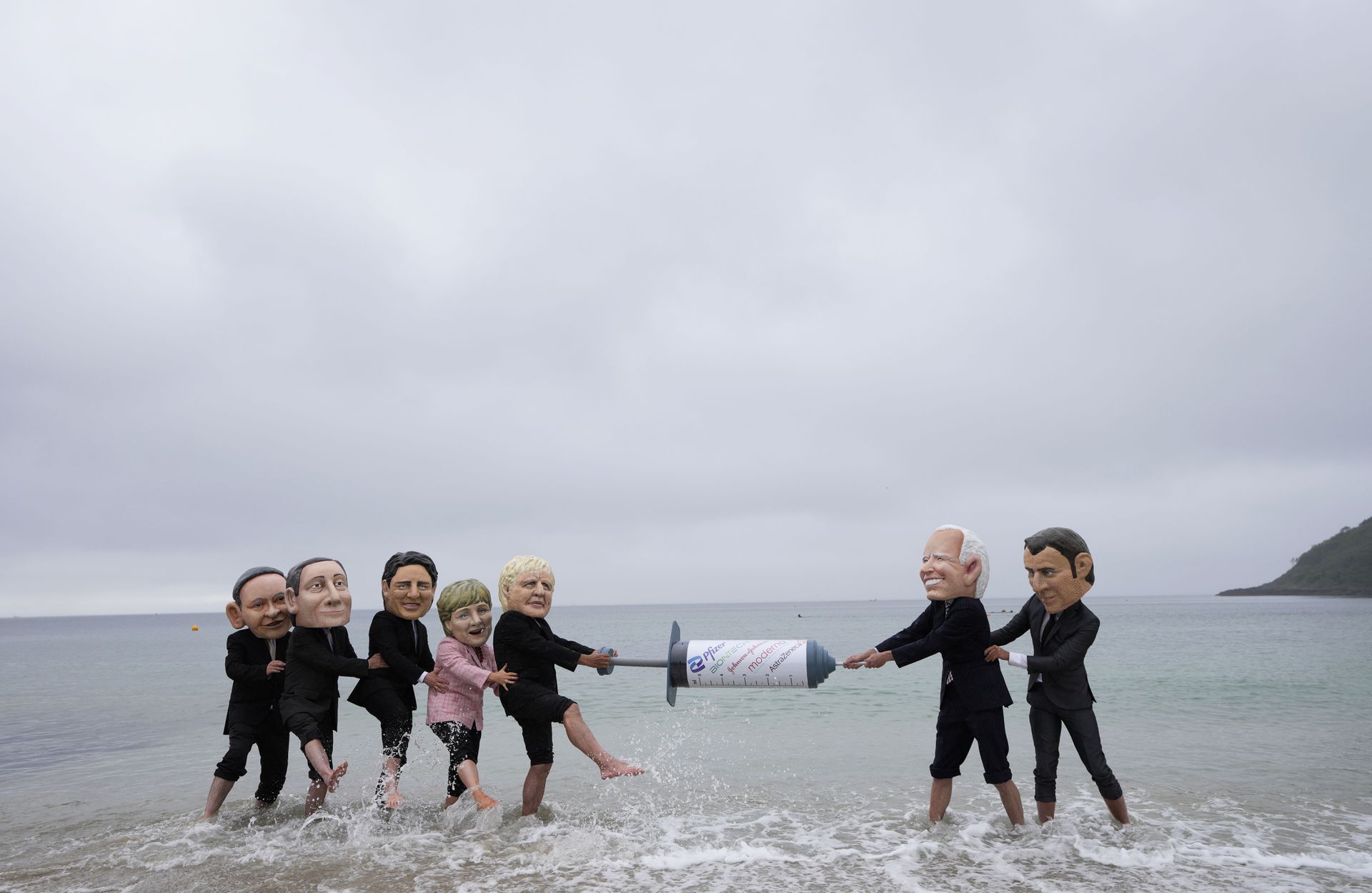 2021 年 6 月 11 日，在英国康沃尔举行的 G7 峰会期间，某NGO在法尔茅斯的 Gyllyngvase 海滩上带着七国领导人的仿真道具举行抗议。画面中，扮演七国领导人的活动家们争抢一个大针筒，以此讽刺G7成员国在疫苗接种问题上反复无常的糟糕表现。（AP）
