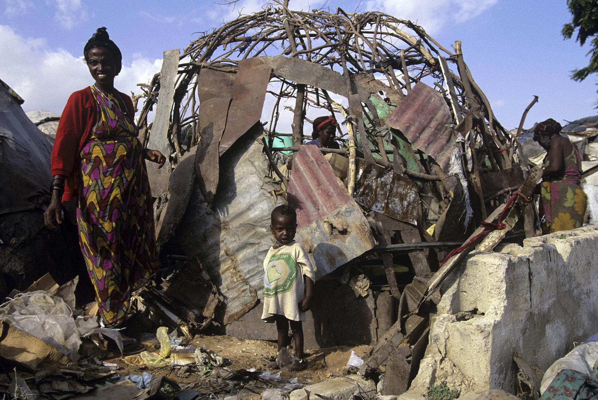1996年12月在卢旺达，一个母亲和儿童站在他们的住房旁边，一个主要由木材和废金属制成的庇护所。（VCG）