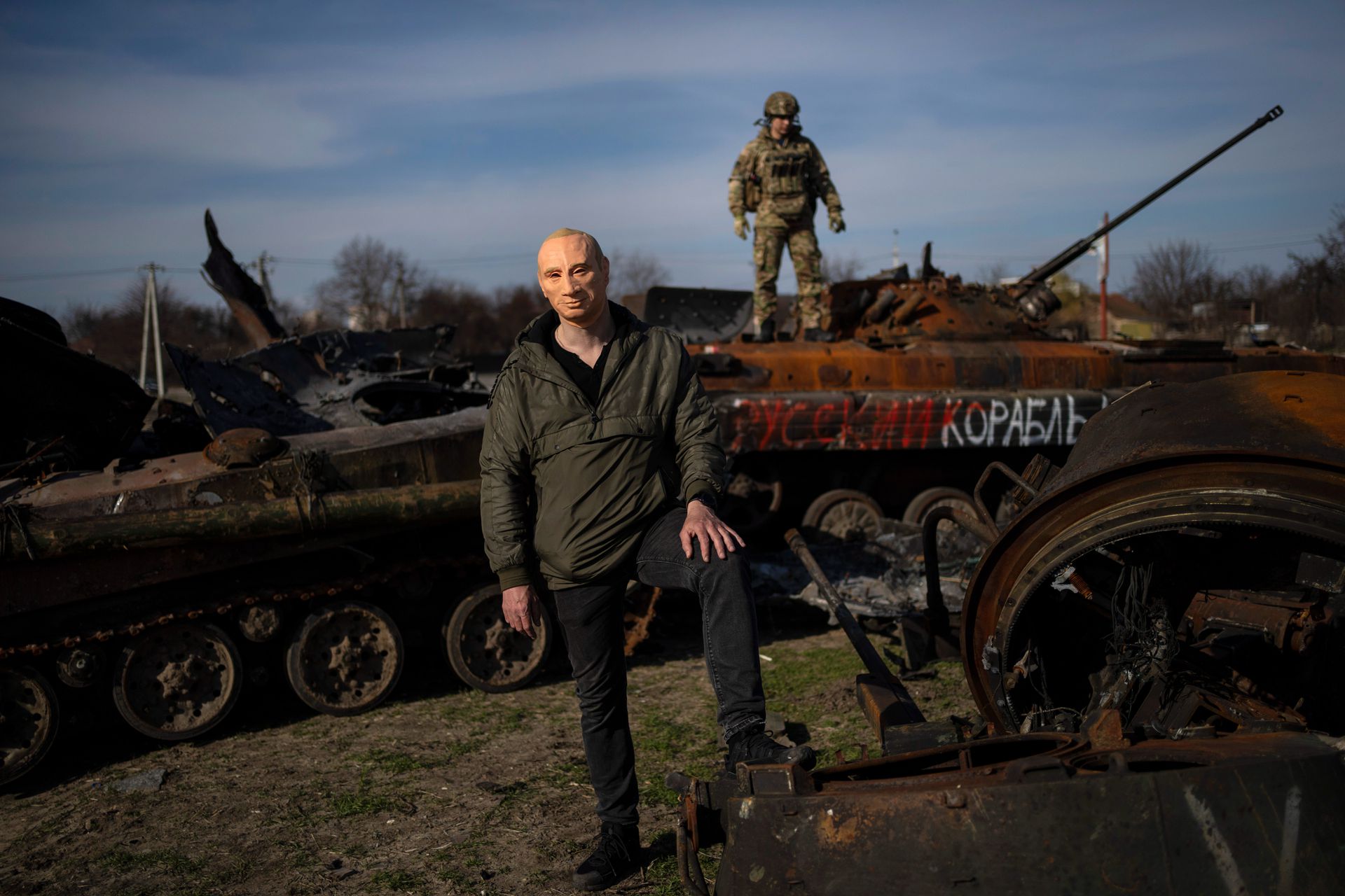 2022年4月7日，在乌克兰首都基辅郊外的布查（Bucha），一名乌克兰士兵站在一辆被摧毁的俄罗斯坦克上，一名男子戴着俄罗斯总统普京的面具拍照。（AP）