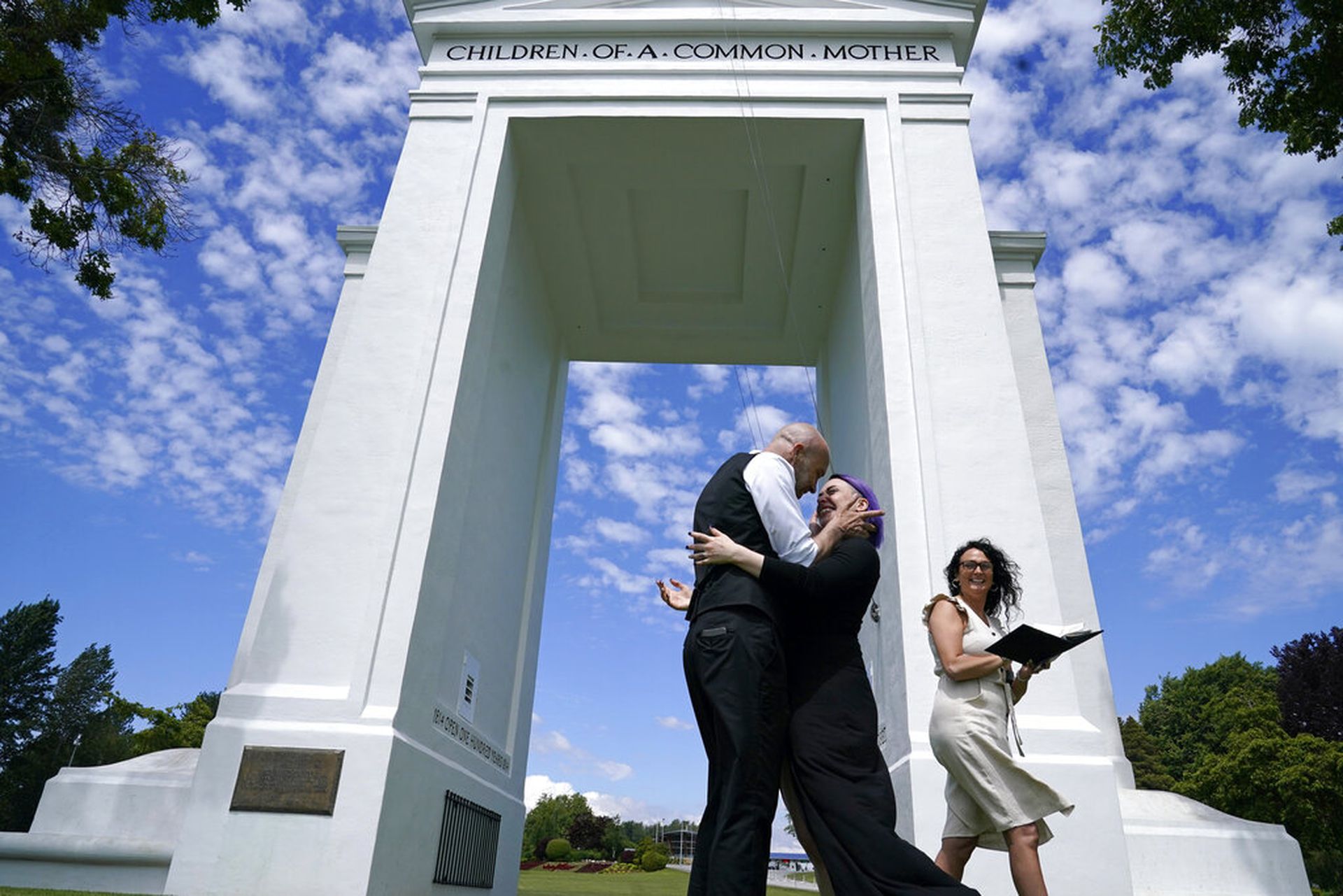 图为一对美加情侣6月8日在和平门国家公园结婚，两人在分隔美加的拱门下拥抱。后方职员此时笑着走开，将时间留给这一对新人。这个关卡在2020年3月已不再供人作必要的出行之用，不过加拿大人仍可走去这个位于美国的公园，以及在此举行婚礼。（AP）