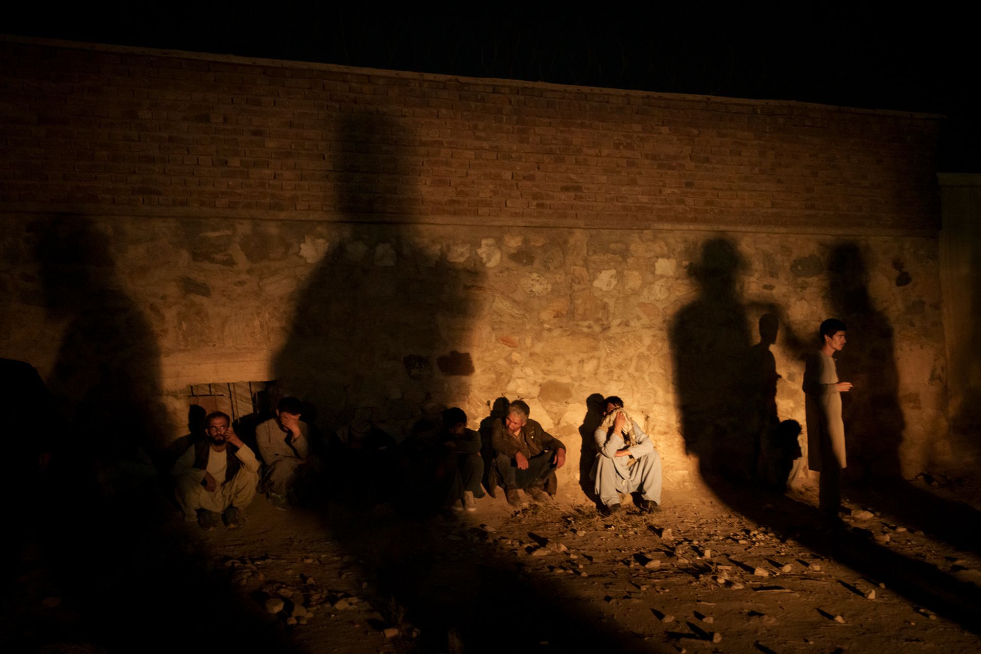 10月1日，阿富汗喀布尔，塔利班武装分子的影子投射在警署的墙上，而墙边则坐着被扣押的吸毒犯。（AP）