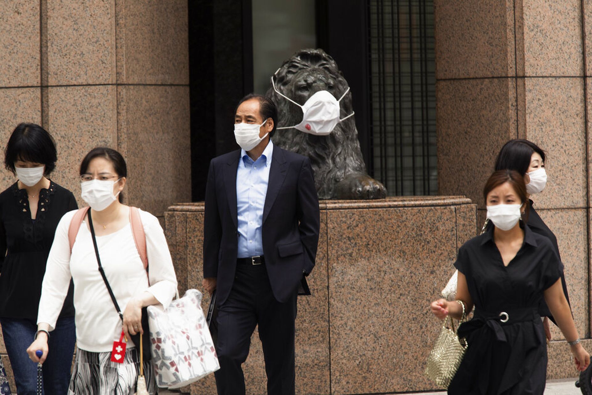 日本新冠肺炎疫情：图为5月21日日本东京的民众在过马路，他们身后一只狮子雕像被戴上口罩。（AP）