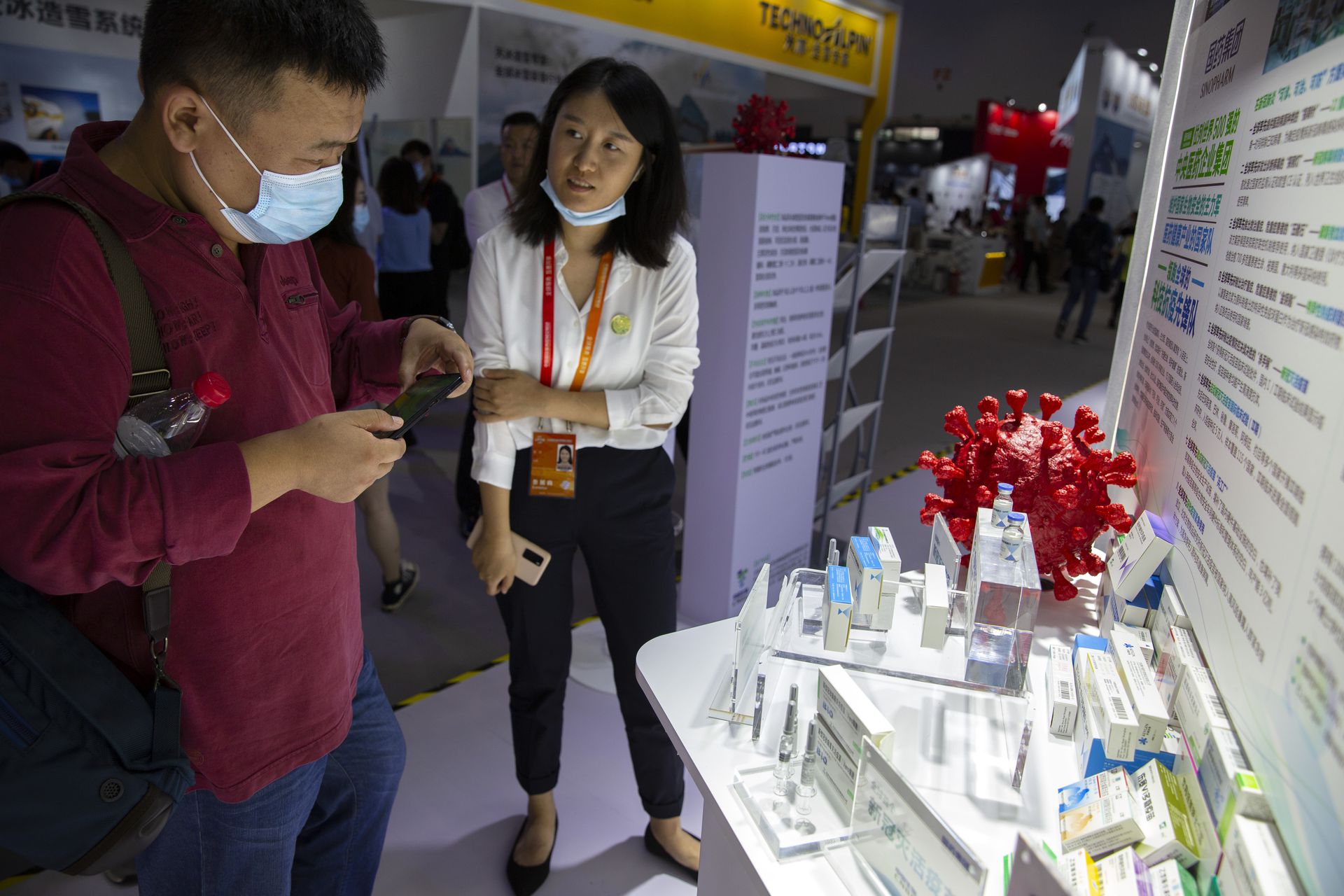 一名工作人员向参观民众介绍中国生物展出的两个新冠病毒灭活疫苗。（AP）