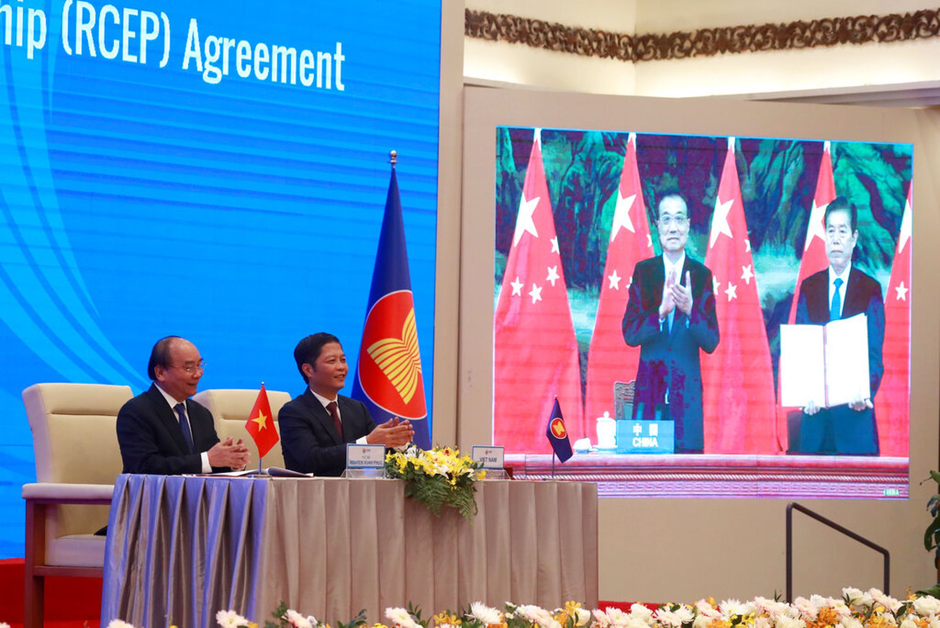 在RCEP签字仪式现场，越南总理阮春福与越南工贸部部长陈俊英鼓掌，中国国务院总理李克强与中国商务部部长钟山出现在大屏幕上。（AP）