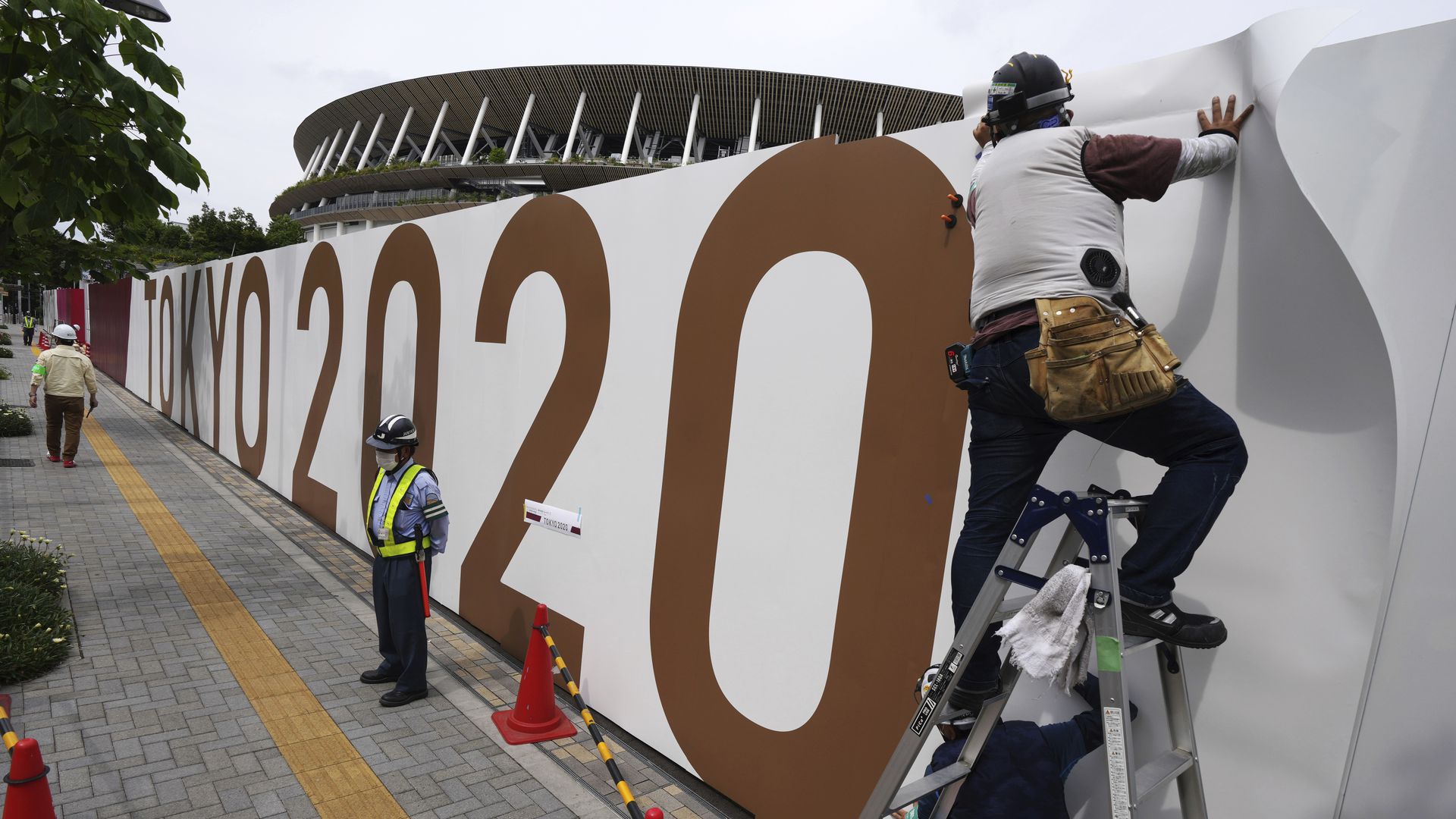 日本新冠肺炎疫情：图为6月2日，日本东京工人为国立竞技场的外墙贴上东京奥运的宣传海报。（AP）